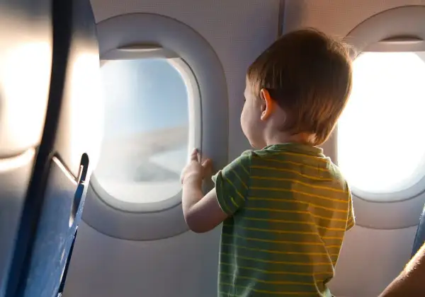 Liten pojke med randig tröja tittar ut genom flygplansfönstret. En magisk upplevelse att flyga med barn.