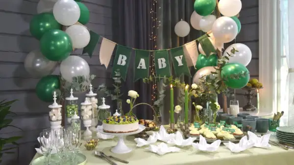 Grön och vit baby shower-dekoration med ballonger, en "BABY"-banderoll, tårta, cupcakes och godis.